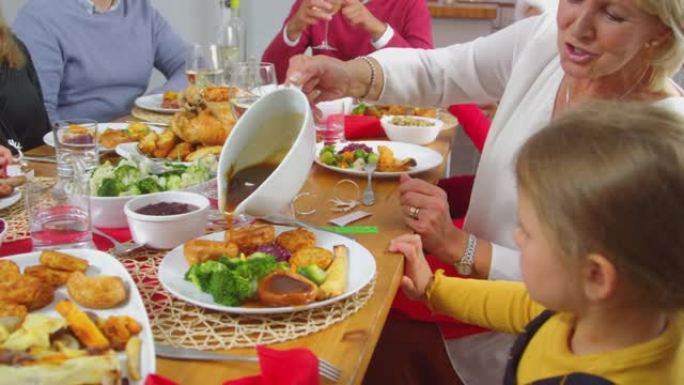 当多代家庭吃圣诞大餐时，祖母将肉汁倒在孙女的食物上