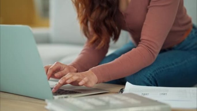 女人，手和笔记本电脑坐在家里沙发上的客厅桌子上打字商务电子邮件。在计算机上远程工作的创造性女员工的手