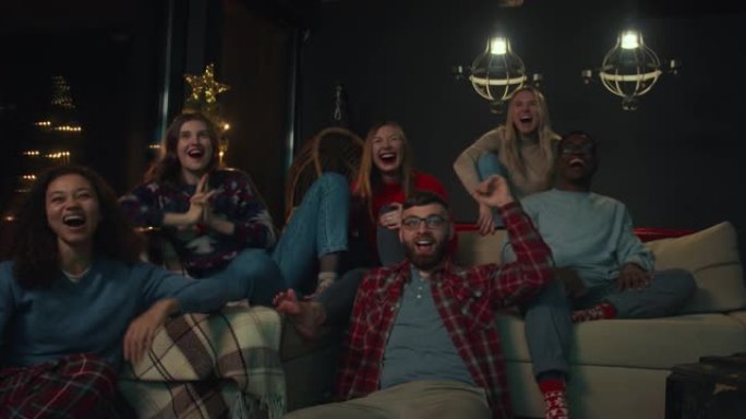 快乐的年轻兴奋的多民族朋友在电视上观看体育节目，在圣诞晚会上大喊大叫，举手慢动作。