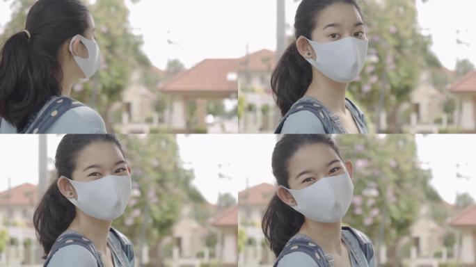 在屋外的白天，美丽的亚洲少年女孩的肖像清晰地在面具后面微笑。可爱的女孩戴着外科口罩，防止病毒或空气污