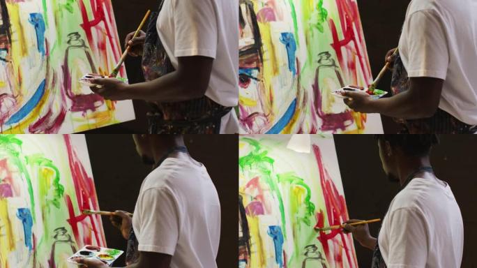 非裔美国男艺术家在艺术工作室穿着围裙画，画笔画在画布上