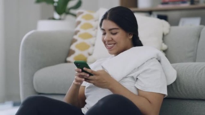在客厅进行家庭锻炼后，大码女士在手机上发短信。微笑的年轻胖女人使用技术浏览互联网和社交媒体。在减肥应