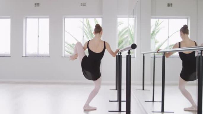 在明亮的工作室里，白人女芭蕾舞演员在镜子前伸展