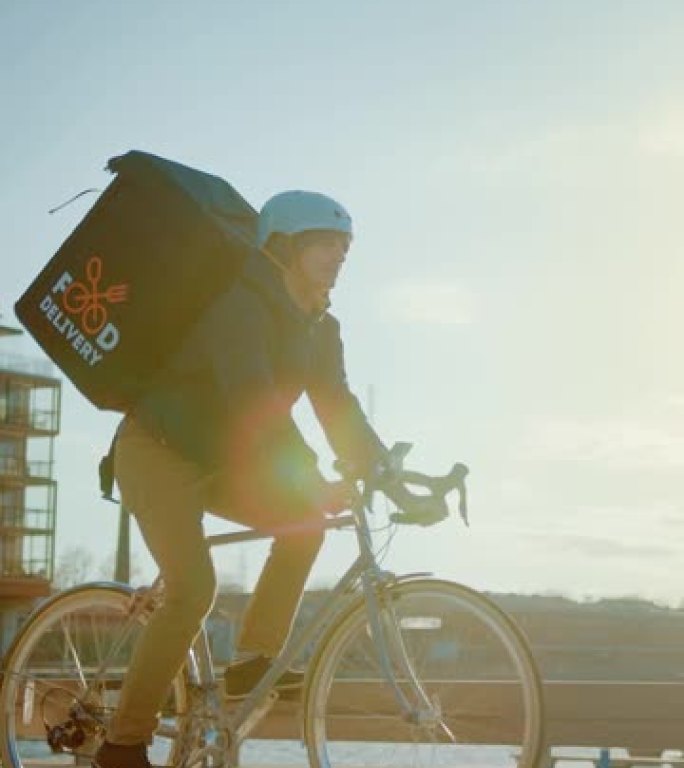 快乐食品配送快递员穿着保暖背包骑着自行车在路上为客户配送订单和包裹。晴天。垂直屏幕方向9:17的视频