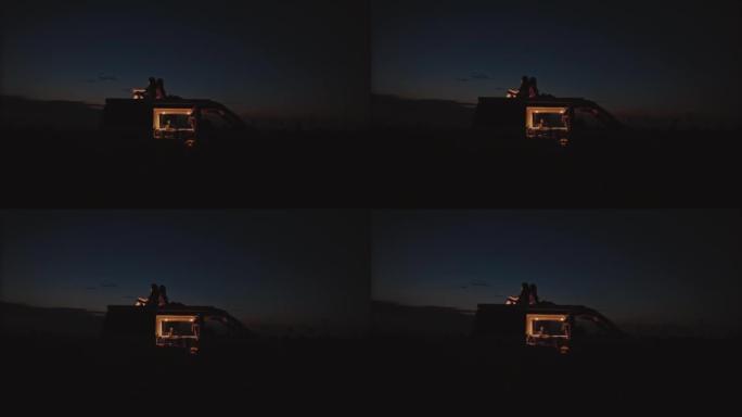 DS两名妇女晚上在田野中央背靠背坐在露营者的屋顶上
