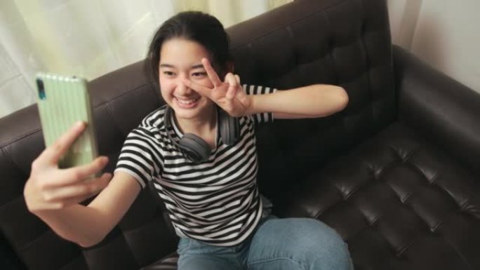 年轻的亚洲女孩在家里的客厅为社交媒体拍照自拍。自画像