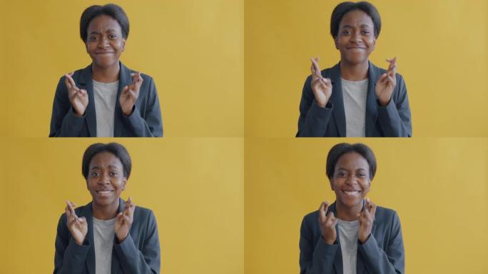 充满希望的年轻非洲裔美国妇女交叉手指许愿并微笑的肖像