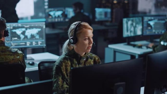 女性军事监视官在中央办公室中心的耳机上交谈，以进行网络操作，控制和监视，以管理国家安全，技术和军队通