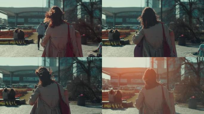 镜头跟随美丽的棕色头发的女人，穿着优雅的米色秋衣，沿着风城街道慢动作行走。