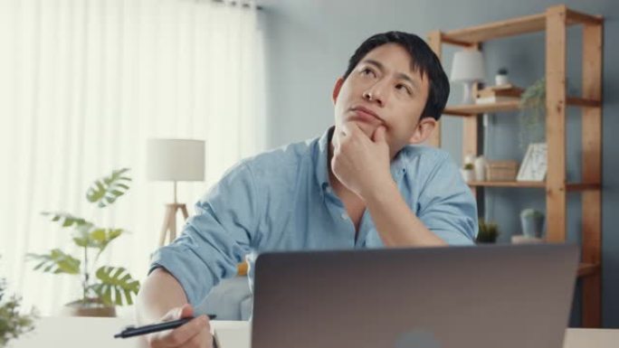 自由职业者亚洲男休闲服在家庭办公室的客厅使用笔记本电脑在线。