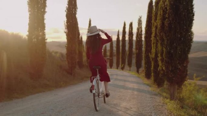 在托斯卡纳的柏树林立的道路上，SLO MO女人骑着复古的自行车