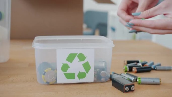 女性手将旧废旧电池放在家里带有回收符号的容器中