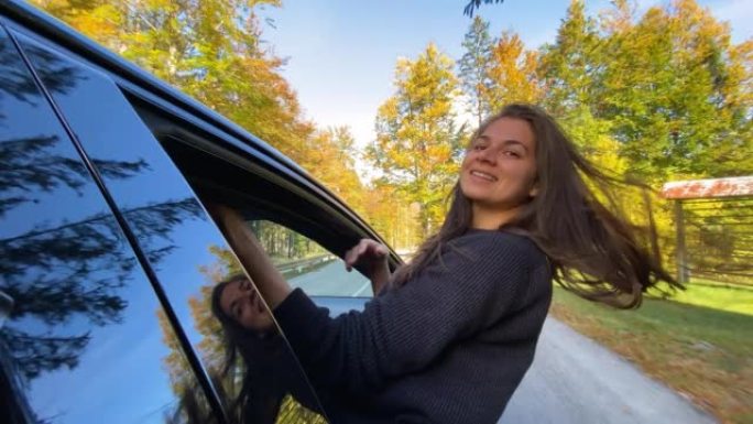女人玩得开心，开车穿过秋天的森林时从车窗外倾斜