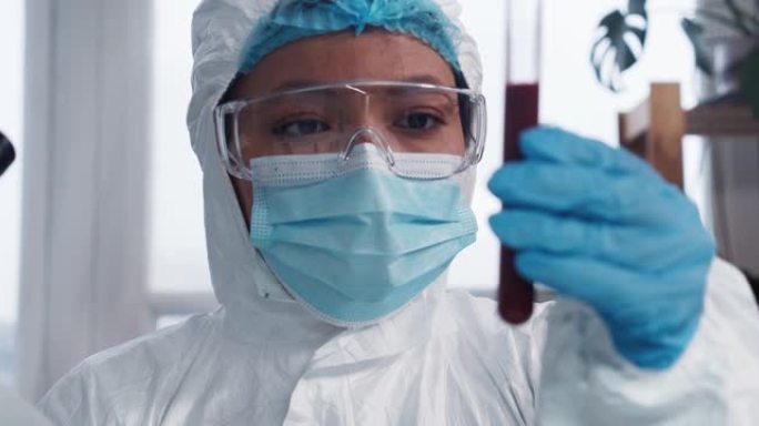临床试验。年轻的专注于混合种族制药实验室医生科学家在防护服中看着血液试管。