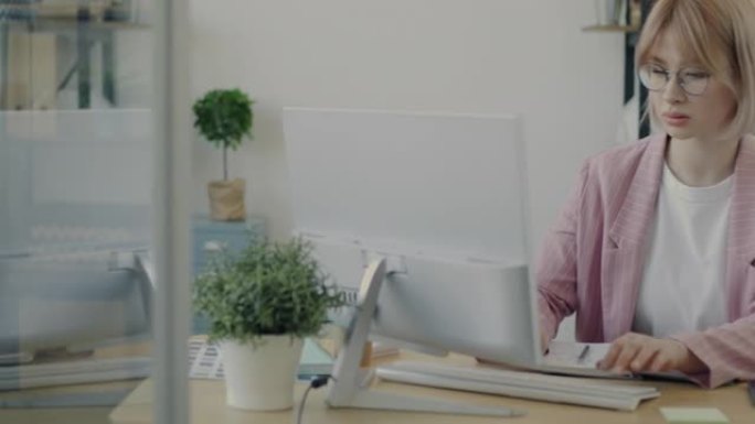 在现代玻璃墙办公室从事计算机打字工作的严肃年轻企业家的肖像