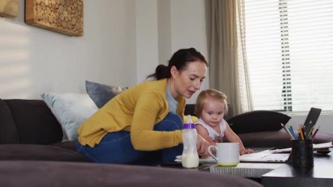 白人母亲在家工作时用笔记本电脑抱着婴儿做笔记