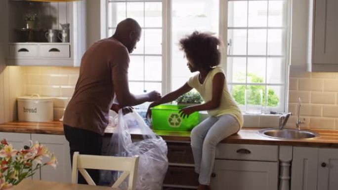 非裔美国女儿和她的父亲在厨房里一起整理回收