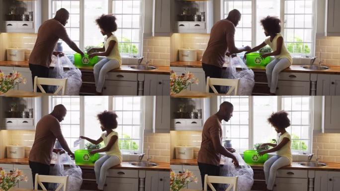 非裔美国女儿和她的父亲在厨房里一起整理回收