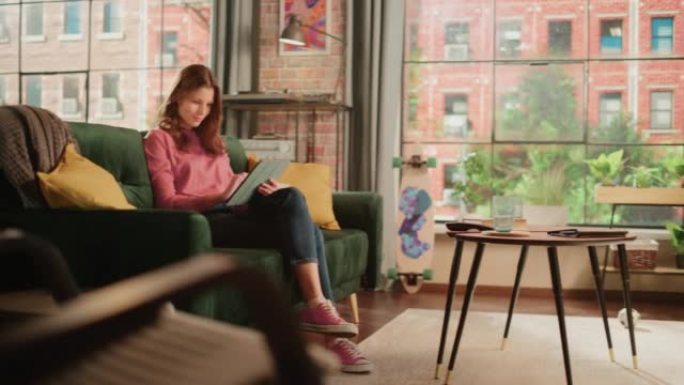 年轻漂亮的女性坐在阁楼公寓的沙发上，在家用平板电脑工作。有创造力的女人检查社交媒体，浏览互联网。从大