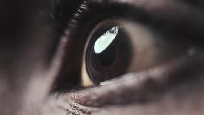 非裔美国人的眼睛在特写镜头中看着光线。眼睑和睫毛下深色虹膜和瞳孔的宏观缩放图像。抽象黑人室内的真实角