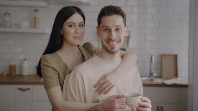 男人和女人站在厨房里抱着咖啡杯微笑的慢动作肖像