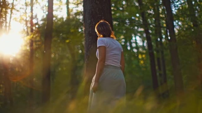 穿着白色长裙的SLO MO女人在森林中走向阳光时抚摸树木