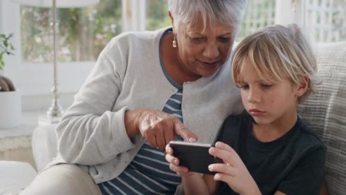 快乐的小男孩使用智能手机展示奶奶如何使用手机教学奶奶现代技术智能孩子在家帮助奶奶4k