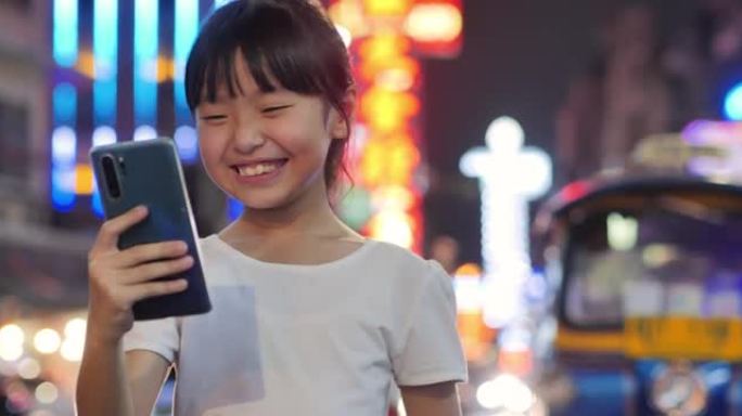 10岁的亚洲女孩的幸福在夜晚的城市中使用带有5g的手机。可视化5g概念