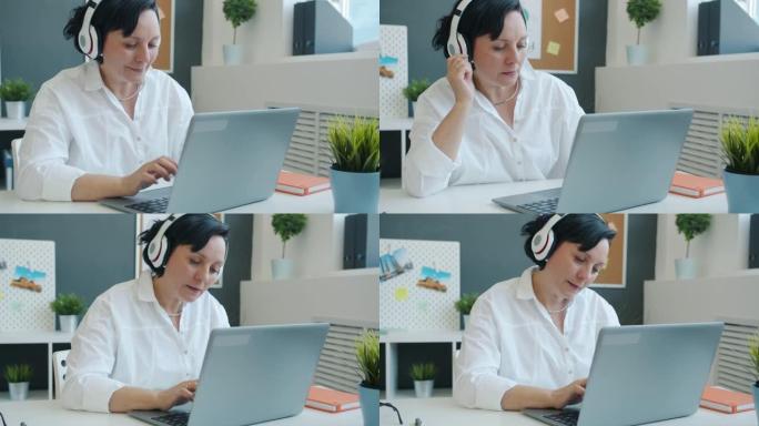 快乐的女商人在办公室里用笔记本电脑工作，通过耳机享受音乐