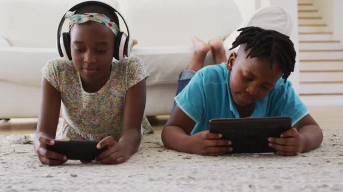 非裔美国人兄弟姐妹在家中使用电子设备躺在地板上