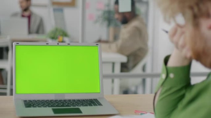 办公室桌上的色度键绿屏笔记本电脑的特写镜头和看显示器的人