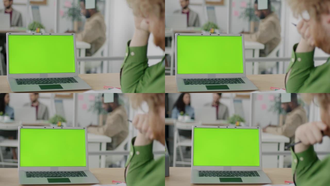 办公室桌上的色度键绿屏笔记本电脑的特写镜头和看显示器的人