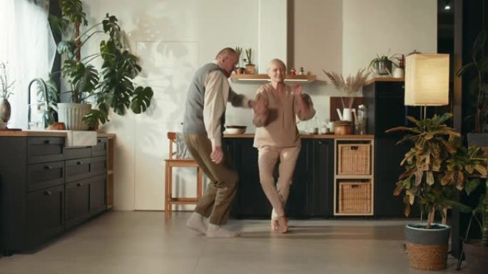 忠诚概念。快乐甜蜜65-70岁的高级男人和女人一起跳舞，在舒适的厨房里大笑。