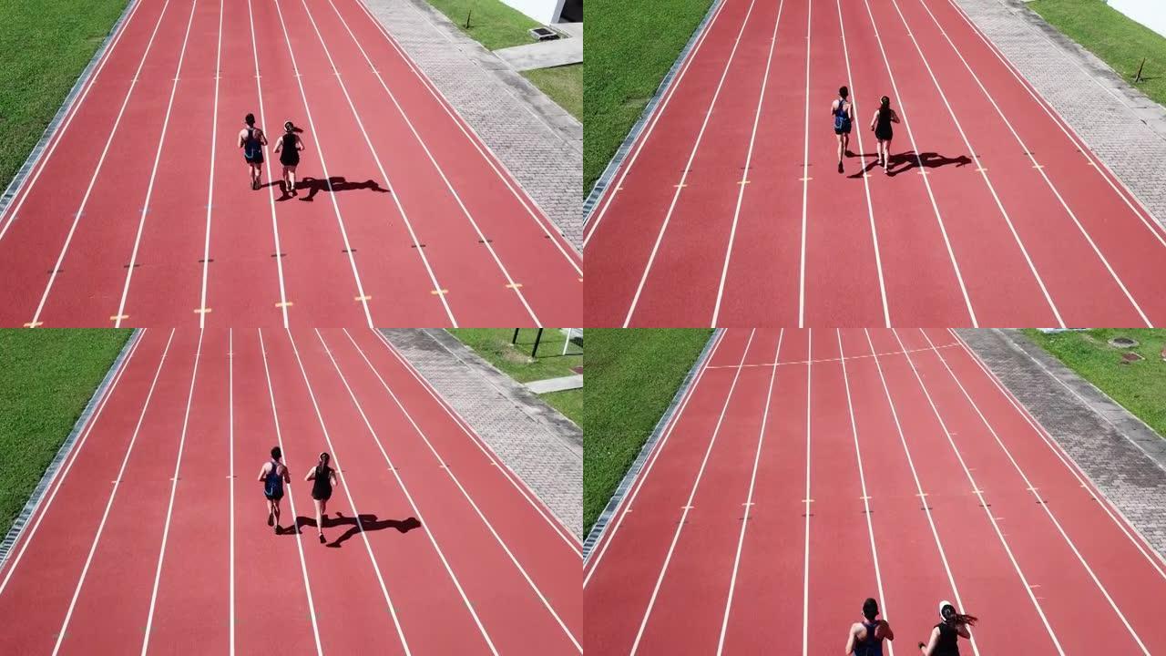 无人机视点运动亚洲华裔情侣运动员上午在田径场跑步
