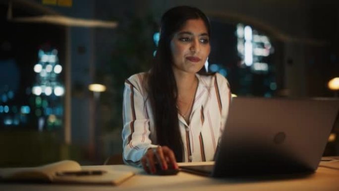 晚上在公司办公室里，一位美丽的印度女性在笔记本电脑上工作的肖像。年轻的秘书分析报告。客户经理为客户制