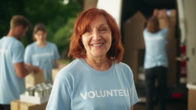 一位快乐乐于助人的中年女志愿者的肖像。成年白人妇女穿着蓝色t恤，微笑着看着相机。人道主义援助、捐赠中