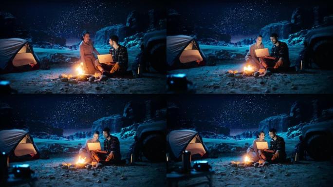 晚上在峡谷里露营的帐篷: 男人坐在篝火旁使用笔记本电脑，他的女朋友加入了他的行列。他们观看流媒体服务