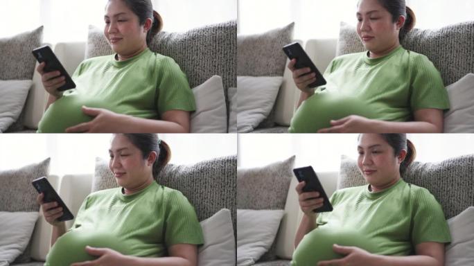 穿着绿色西装的孕妇在家中客厅沙发上使用手机