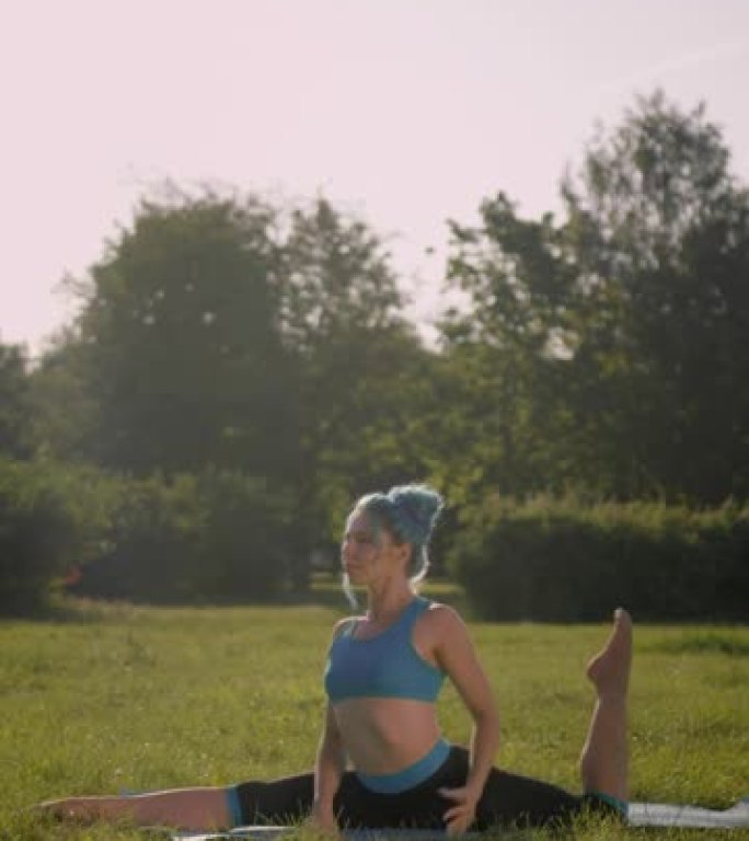 垂直视频，一位迷人的健身瑜伽老师穿着绿松石的头发，穿着绿松石的瑜伽服装，用弯曲的后腿做纵向麻线