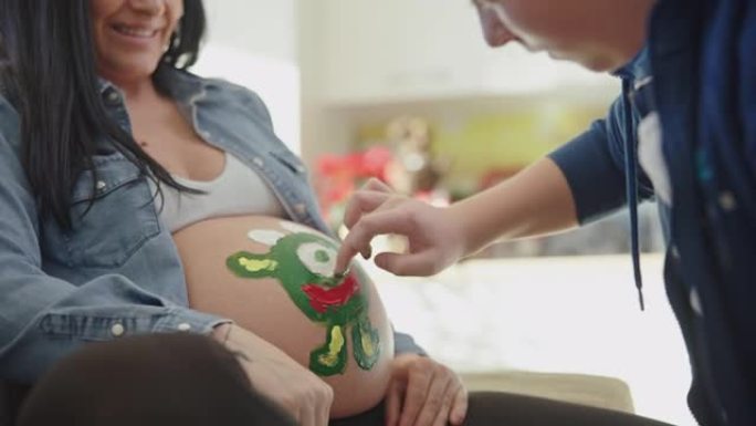 一个十几岁的男孩在一位母亲怀孕的肚子上用手指作画