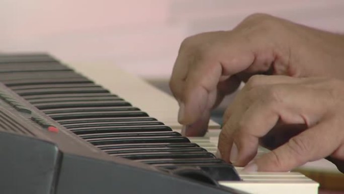 男老师坐在电钢琴上，在阿根廷布宜诺斯艾利斯的一所公立小学为学童上音乐课。特写。