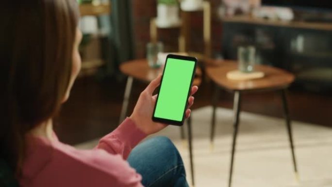 女性手握着带有绿屏模拟显示的智能手机。女性在家里放松，在移动设备上观看视频和阅读社交媒体帖子。特写镜