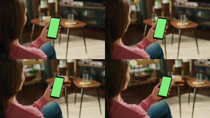 女性手握着带有绿屏模拟显示的智能手机。女性在家里放松，在移动设备上观看视频和阅读社交媒体帖子。特写镜
