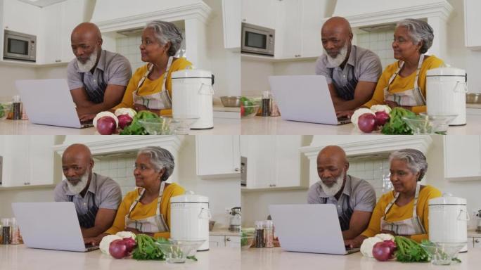 非裔美国老年夫妇在家里的厨房里一起穿着笔记本电脑围裙