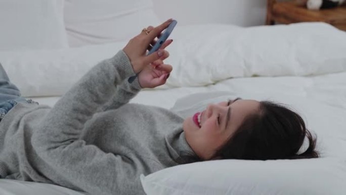 年轻漂亮的女人躺在床上用手机