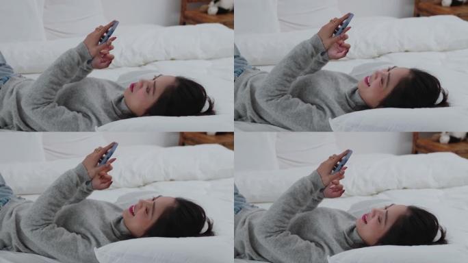 年轻漂亮的女人躺在床上用手机
