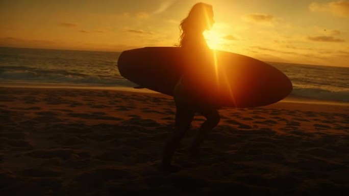 日落时分，长发的年轻女子在海滨行走，手臂下背着冲浪板