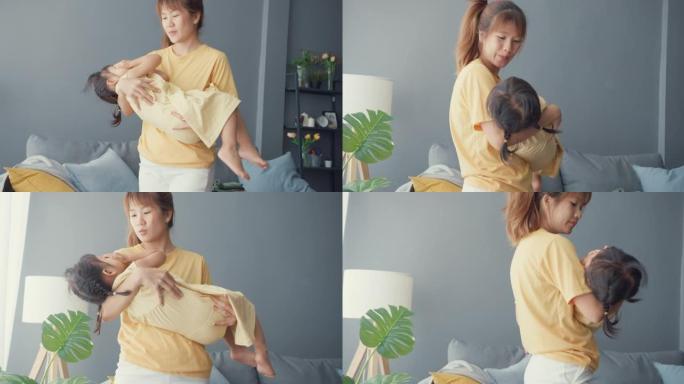 快乐快乐的亚洲家庭妈妈抱着蹒跚学步的女孩哭泣，舒适地护理在家里的客厅行走。