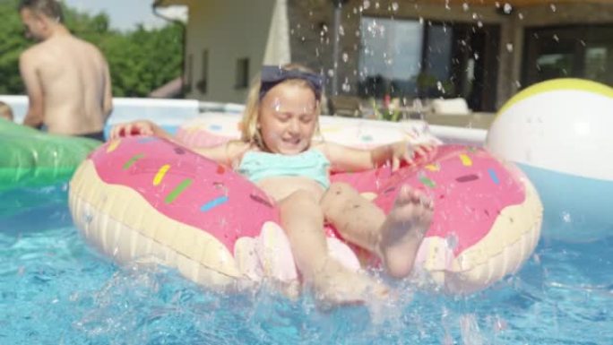 关闭小女孩一边泼水，一边漂浮在游泳池里的漂浮甜甜圈上
