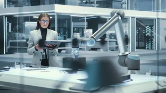 年轻漂亮的女工程师使用平板电脑，在高科技工业实验室中研究和开发具有现代设备的未来派机械臂机器。电影镜